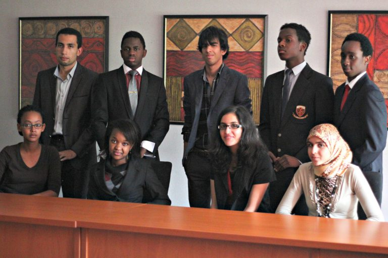 Eight people in business attire pose in a conference room. They sit and stand with neutral expressions, framed by abstract art on the walls.