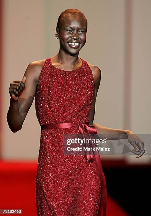 Smiling person in a sparkling red dress walks a runway. The background is blurred; mood is joyful and confident.